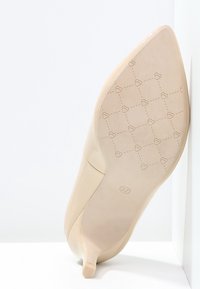 Beige korkeakorkoinen kenkä, jossa on terävä kärki, sileä päällinen ja kuvioitu pohja, jossa pieniä sydämiä, koko merkitty 37.