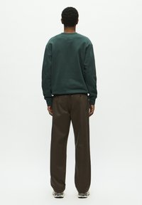 Dark green sweatshirt with a round neck, paired with brown wide-leg pants. The fabric appears soft, with a casual fit. Sneakers visible.