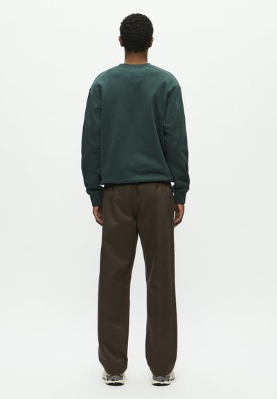 Dark green sweatshirt with a round neck, paired with brown wide-leg pants. The fabric appears soft, with a casual fit. Sneakers visible.