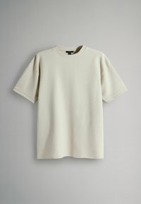 T-shirt beige clair à manches courtes en tissu côtelé doux avec un col rond et une coupe légèrement oversize. Design épuré et simple sans motifs.
