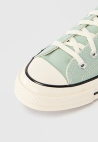 Πράσινο πάνινο αθλητικό παπούτσι με εκρού ελαστική μ ύτη, μαύρο περίγραμμα και μπεζ κορδόνια. Διαθέτει ασημένιες τρύπες για τα κορδόνια και υφασμένο πέλμα.