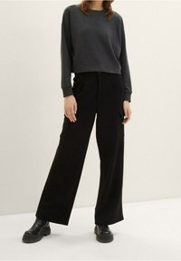 Sudadera gris de manga larga combinada con pantalones de pierna ancha negros de cintura alta y botas negras gruesas sobre un fondo neutro.