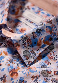 Bloemenpatroon shirt met een lichtblauwe achtergrond en oranje en zwarte accenten. Opvallende kraagtextuur en label zichtbaar.