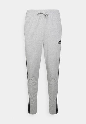 Pantalon de jogging gris avec une taille élastique et un cordon de serrage, des bandes noires sur les côtés et un logo Adidas sur la cuisse gauche.