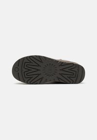 Semelle de chaussure marron avec motifs géométriques profonds, motif circulaire au centre et petit logo circulaire près du talon.
