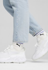 Baskets blanches avec des empiècements texturés, des lacets et des semelles épaisses. Portées avec un jean en denim bleu clair et des chaussettes blanches avec des accents de logo noirs.