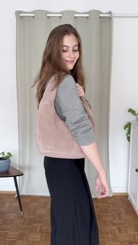 Lys rosa, ærmeløs vest med en blød tekstur, afrundede kanter, båret over en grå langærmet top; parret med sorte bukser.