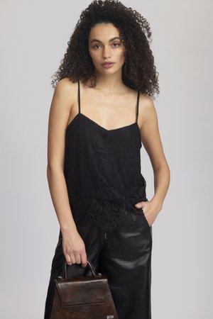 Top de encaje negro con tirantes finos, que presenta un patrón floral texturizado, combinado con pantalones de cuero negros de cintura alta y un bolso marrón oscuro.