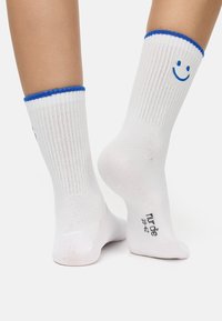 Hvide ribbede sokker med blå detaljer ved kanten og et blåt smilende ansigt design. Inkluderer trykte størrelsesoplysninger under buen.