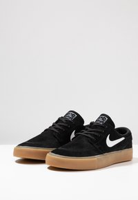 Scarpe da skate in suede nero con logo Nike swoosh bianco, lacci piatti e suola in gomma; presentano una finitura liscia e un design semplice.