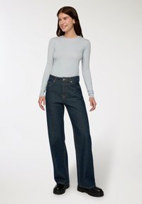 Maglia azzurro chiaro a maniche lunghe, aderente al torso. Jeans in denim scuro a gamba larga con cuciture arancioni e tasche frontali. Scarpe con tacco nero.