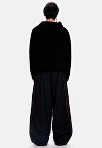 Juodas pūkuotas džemperis su gobtuvu, derinamas su laisvais juodais kelnėmis, kurių šonuose yra raudonos detalės. Apranga pasižymi laisvu, patogiu siluetu.