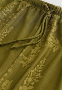 Olivgröna byxor med en texturerad blommönster, utrustade med en elastisk midja och justerbart snöre för en säker passform.