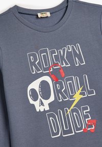 Sudadera de algodón gris con un diseño gráfico que incluye texto, una calavera, auriculares rojos, un rayo amarillo y notas musicales.