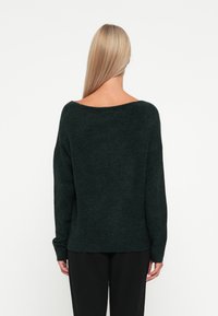 Donkergroene, oversized trui met een brede halslijn, geribbelde manchetten en zoom, gemaakt van zacht, textuur materiaal. Achteraanzicht weergegeven.