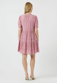 Light pink lace dress with puff sleeves, tiered skirt, and scalloped hem, featuring intricate cutout patterns and a fitted bodice.