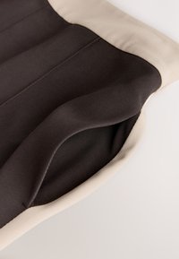 Prim-plan al unei săculețe din material negru cu bordură bej, prezentând interiorul deschis și cusăturile detaliate.