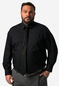 Zwarte langemouwen shirt met een button-down kraag, enkele borstzak en een bijpassende stropdas. Draagt met grijze broeken en een leren riem in bruin.