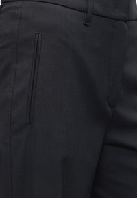 Κοντινό πλάνο μαύρου παντελονιού που δείχνει πλαϊνή κατακόρυφη τσέπη και μέρος της μέσης με θηλιά για ζώνη.