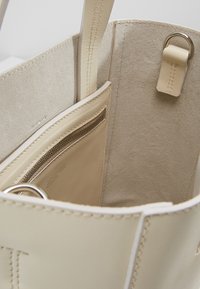 Beige läder tote-väska inuti med en mockafodring, ett dragkedjefack och grå sömmar. Inkluderar en metallslinga som detalj.