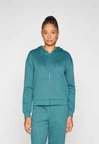 Φούτερ με φερμουάρ σε αποχρώσεις τυρκουάζ, με κουκούλα και κορδόνι, τσέπες καγκουρό, ριμπ τελείωμα και μανσέτες· κατασκευασμένο από απαλό, υφασμένο ύφασμα.