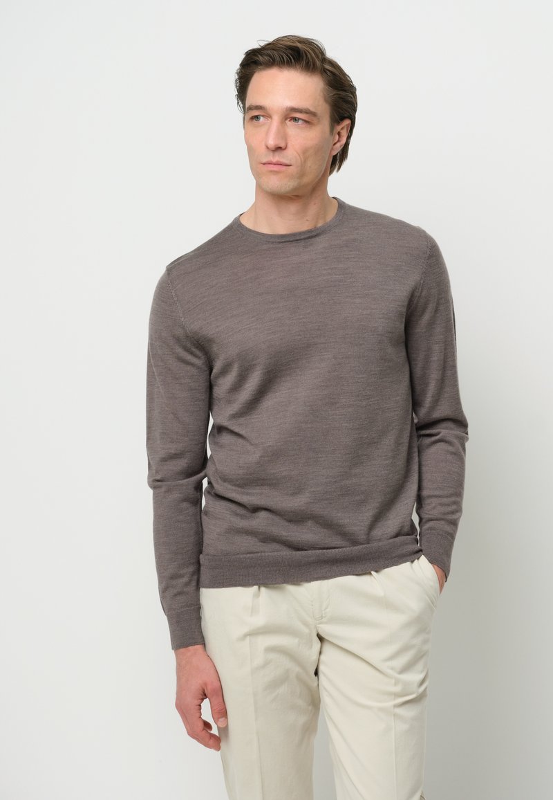 Maglione grigio a maniche lunghe con colletto tondo, realizzato in materiale morbido, con una vestibilità aderente e una sottile trama. Abbinato a pantaloni chiari.