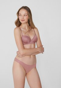 Roze bh met kant en onderdraad, verstelbare bandjes en een bijpassende lage slip met gladde stof en zijaccenten.