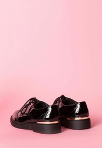 Scarpe stringate in vernice nera con un accento dorato contrastante sul tallone. Presentano una punta arrotondata e dettagli a texture sui bordi.