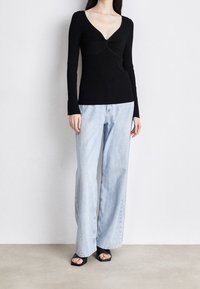 Czarna bluzka z długim rękawem, dekoltem w serek i marszczonym środkiem, zestawiona z jasnoniebieskimi szerokimi jeansami. Czarne sandały na słupku z odkrytymi palcami.