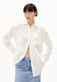 Witte linnen button-up shirt met lange mouwen en een borstzak, gecombineerd met een lichtblauwe denim rok met hoge taille.