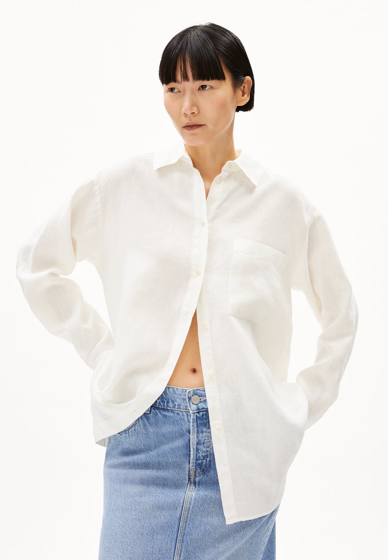 Witte linnen button-up shirt met lange mouwen en een borstzak, gecombineerd met een lichtblauwe denim rok met hoge taille.