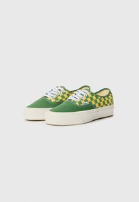 Green and yellow checkered canvas sneakers with white laces, rounded toe, and a cream-colored rubber sole. Flat design, casual style.