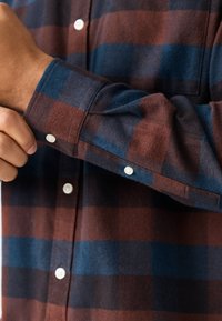 Bawełniana flanelowa koszula z brązowo-niebieskim wzorem w kratę. Długie rękawy z guzikami i miękkie, teksturowane wykończenie.