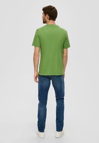 T-shirt verde in cotone con maniche corte e collo rotondo, abbinata a jeans blu di denim e sneakers bianche.