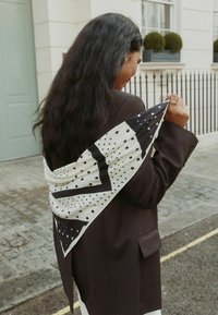 Black and white patterned silk scarf draped over a dark blazer, featuring polka dots and geometric shapes, soft texture and elegant design.