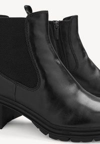Bottines en cuir noir avec une finition lisse, des panneaux latéraux en mesh et un talon bloc bas, équipées d'une fermeture éclair latérale pour un enfilage facile.