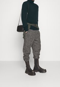 Mörkgrön polo-tröja, mönstrade svart och vita tapered byxor, samt svarta ankelstövlar med tjocka sulor och metalliska accenter.