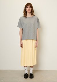 Hallide lühikeste varrukatega hall T-särk, mis on kombineeritud voolava kollase midi seelikuga. Mudel kannab musti loafer'eid ja valgeid sokke mustade tekstidega.