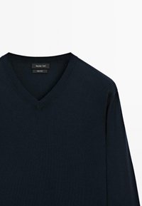 Maglione in cotone blu navy a V con collo a costine. Etichetta visibile all'interno del colletto. Texture liscia, maniche lunghe e design semplice.