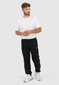 Weißes Baumwoll-T-Shirt mit gelbem Logo, kombiniert mit schwarzen Hose mit elastischem Bund und weißen Sneakers. Lässige, athletic Passform.