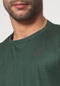 Dark green athletic shirt made from breathable fabric, featuring a subtle perforated pattern and a small black logo on the front.