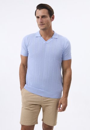 Polo de punto de manga corta azul claro con escote en V, que presenta un patrón texturizado. Combinado con pantalones cortos beige y un corte relajado.