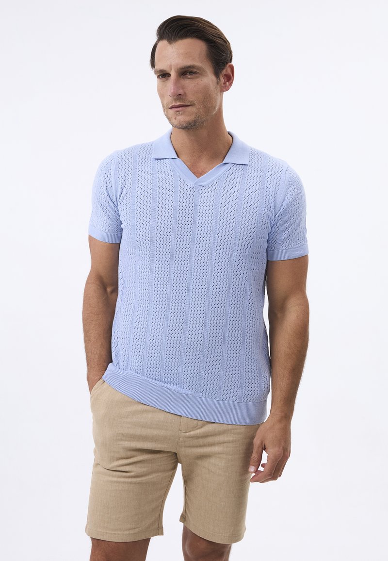 Ljusblå kortärmad stickad polo med v-ringning, som har ett texturerat mönster. Matchad med beige shorts och en avslappnad passform.