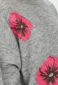 Grauer Strickpullover mit großen rosa Blumenmotiven und dunklen Mittelpunkten. Weicher Stoff, gerippter Halsausschnitt und lockere Passform.