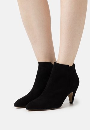 Bottines en daim noir avec un bout pointu et un talon de 5 cm, présentant un design épuré et une couture minimale pour une finition lisse.