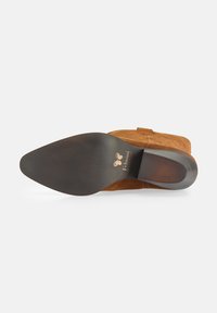 Stivale alla caviglia in suede marrone con punta affilata, suola in gomma nera texture e tacco piccolo. Presenta un logo stampato sulla suola.