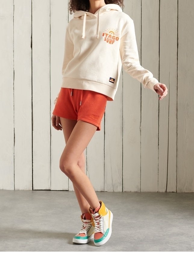 Sweat à capuche beige avec un graphique orange "Itago Surf", associé à un short orange. Baskets montantes multicolores avec des accents verts, jaunes et bruns.