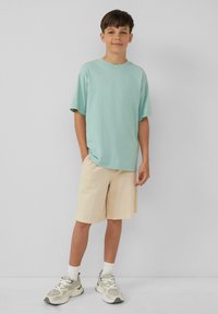 Mintgroene katoenen T-shirt met een relaxed fit, gecombineerd met crèmekleurige gestreepte shorts. Grijze sneakers met witte accenten en witte enkelsokken.