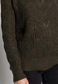 Pull tricoté vert olive avec un motif texturé en torsades. Il comprend des manches longues et un ourlet côtelé, fabriqué à partir d'un fil doux et épais.