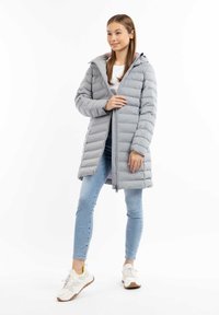 Grå puffjakke med vandret syninger, hætte og lynlås. Bæret over en hvid top, parret med blå jeans og sneakers.